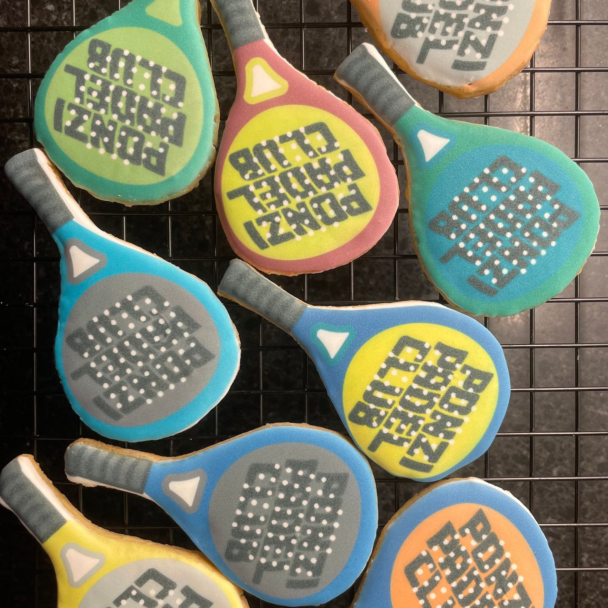 Colorful cookie cutouts shaped like paddle tennis rackets with 'Ponzi Padel Club' text on a grid background.